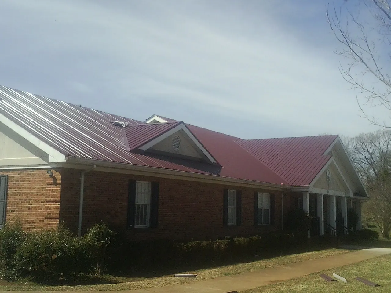 Red metal roof with gabled entries on a long brick building, from a Hail Damage Roof Repair job in Childwold