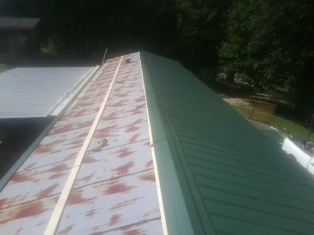 Old rusted panels beside newly installed green metal roofing — Wind Damage Roof Repair by Roofing Brothers in Childwold