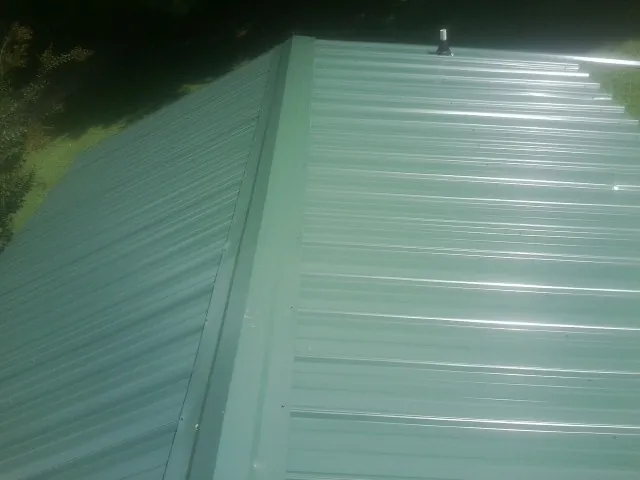 New green metal panels meeting at the ridge of a roof — Flat Roof Repair work by our crew in Childwold
