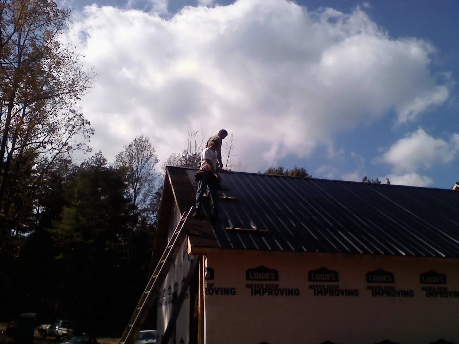 Roofer fastening dark metal panels high against a cloudy sky, from a Roof Inspection job in Childwold