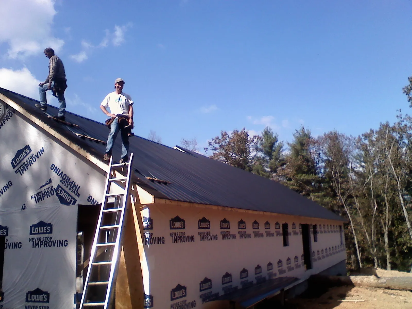 Two roofers standing on a long dark metal roof over a wrapped building in Childwold