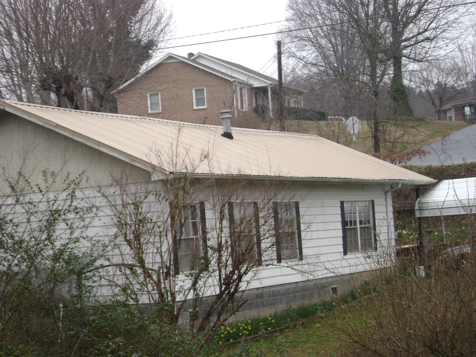 Tan metal roof on a white sided house set into a hillside — Commercial Roofing by Roofing Brothers in Childwold