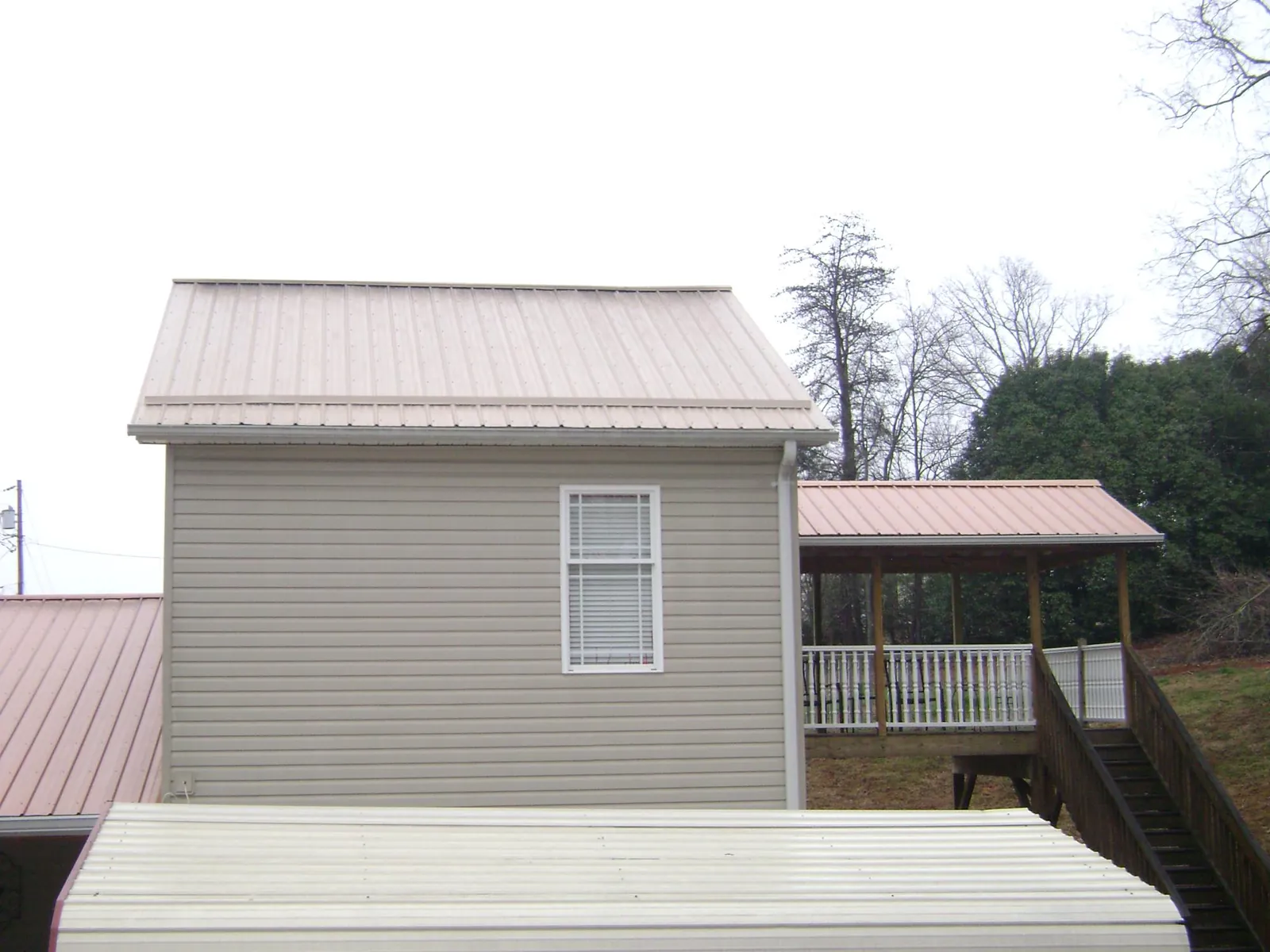 Tan metal roofs on a two story addition and attached porch, from a Roof Replacement job in Childwold